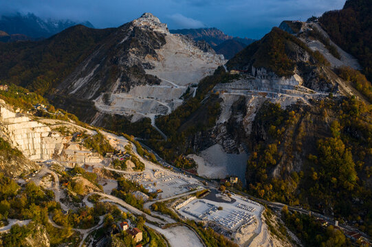 Aerial view of the stark white gashes of marble quarries carve into the verdant mountainsides, creating a dramatic contrast against the rugged landscape, Carrara, Tuscany, Italy.