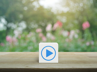 Play button flat icon on white block cube on wooden table over blur pink flower and tree in garden, Business music online concept