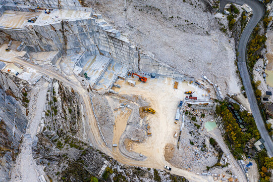 Aerial view of sculpted marble canyons where heavy machinery rests in the stark, bright landscape, a testament to human industry, Carrara, Tuscany, Italy.