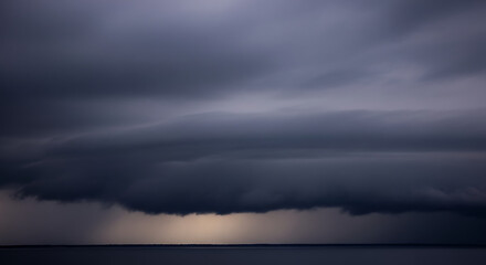 Dramatic dark storm clouds gathering over a calm ocean horizon with subtle light breaking through