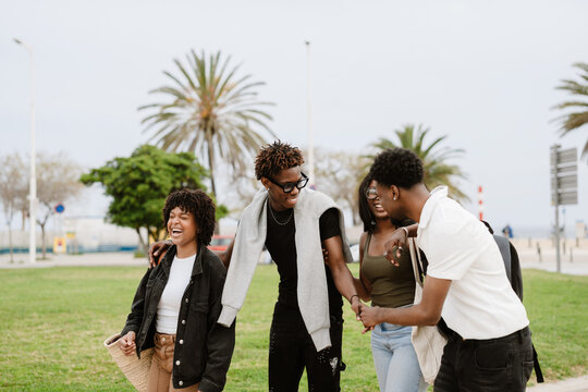 A group of four friends hold each other as they walk and laugh while two of them shake hands - Powered by Adobe
