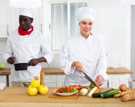 Young woman chef in white uniform working with male colleague in private kitchen