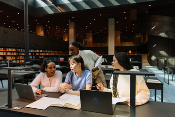 A female student holds a notebook while standing next to a group of three female students sitting...