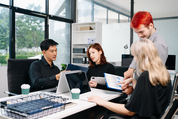 Diverse business team collaborating in a meeting with laptops, tablets, and reports, symbolizing...