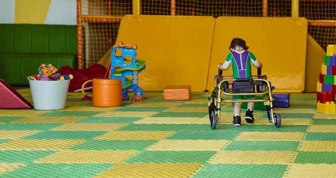 Young child with motor disorder is hard engaged in physical rehabilitation using rehab walker to learn to walk. Physiorehab