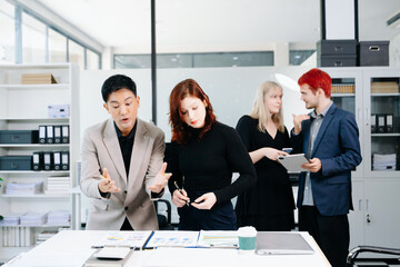 Diverse business team collaborating with laptops, tablets, and reports in a modern office,...