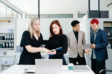 Diverse business team collaborating with laptops, tablets, and reports in a modern office,...