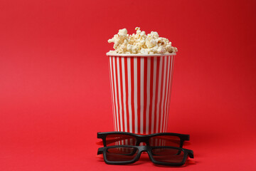 Classic red and white striped box filled with delicious, fluffy popcorn, 3D glasses on a red background.
