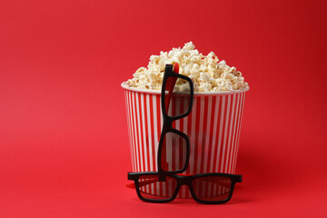 Classic red and white striped box filled with delicious, fluffy popcorn, 3D glasses on a red background.
