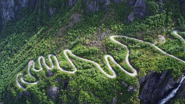 Aerial view of the serpentine Lysevegen road snaking through lush green mountainsides, a striking contrast against the rugged terrain, Lysebotn, Rogaland, Norway.