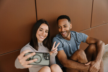 Male and female athletes smiling and looking at the phone she is holding while leaning on the wall...