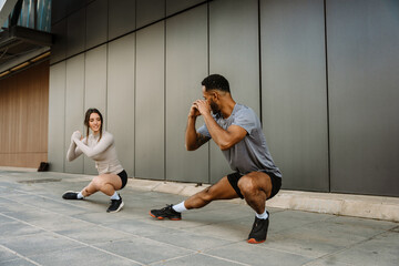 Male and female athletes holding hands together in front of them while squatting and stretching...