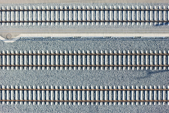 Aerial view of parallel train tracks cutting through a grey stone bed, a stark contrast of industrial precision and natural texture, Deutschlandsberg, Styria, Austria.