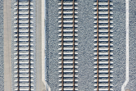 Aerial view of parallel train tracks slicing through a landscape of gray gravel, creating a stark contrast of lines and textures, Deutschlandsberg, Styria, Austria.