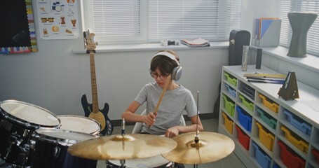 Primary School Boy Wearing Headphones Practicing Drums in Modern Music Class, Dreaming to Become Drummer. Talented Young Boy Playing Drum Set During Percussion Lesson. Rhythm Education, Musical Art.