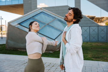 A female athlete is warming up and smiling while looking at a male athlete standing next to her with his eyes closed and his hand on his chest