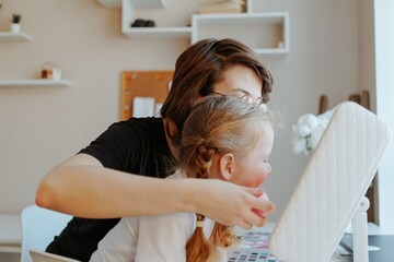 A young mother and her 3-year-old daughter play dress-up as makeup artists, sharing laughter and...