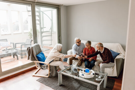 A group of four friends clink glasses and laugh while three of them sit on a sofa and one of them sits on a chair