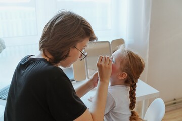 A young mother and her 3-year-old daughter play dress-up as makeup artists, sharing laughter and creativity. A heartwarming scene of role-playing, bonding, and joyful motherhood