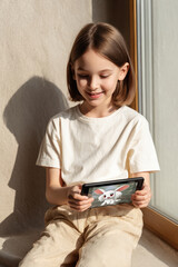 cheerful girl sits on windowsill eagerly engaging with her augmented reality game featuring playful digital pet