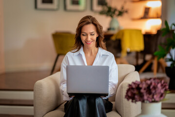 Confident woman with laptop sitting in an armchair at home and working