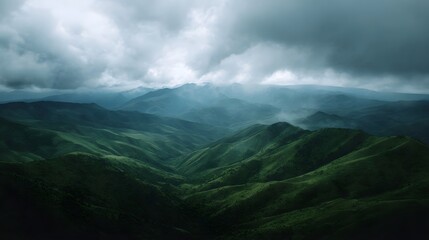 Vast green mountain ranges stretch under a dramatic cloudy sky creating a moody landscape