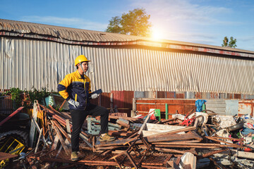 Construction Worker in Safety Helmet Standing Amidst Piles of Scrap Metal and Debris at a Construction Site During Sunset