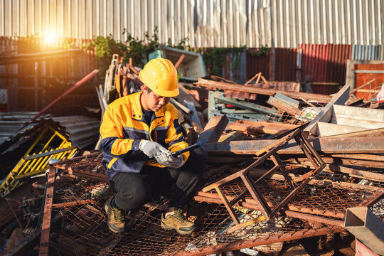 Construction worker inspecting metal scraps in a yard during sunset, wearing a helmet and gloves, surrounded by discarded materials, safety first