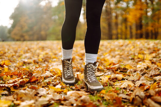 A close-up of a hiker's feet in hiking boots walking along a trail strewn with yellow leaves. A woman in heavy boots enjoys an autumn day in the forest. Concept of walking, hiking. Autumn day!