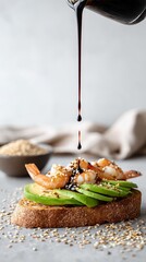 Gourmet whole grain toast topped with avocado slices, shrimp, sesame seeds and drizzled with thick soy or balsamic sauce. A clean, minimal food styling with focus on texture and motion.