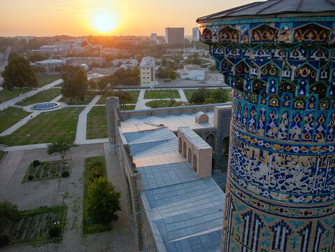 Aerial view of a minaret with intricate blue tile work glows in the warm light of the setting sun over the cityscape, Tashkent, Uzbekistan.