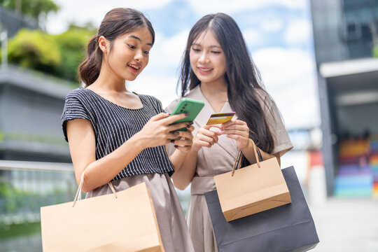 Two asian woman shopping outdoors using credit card and smartphone for mobile payment, concept of cashless society, online transaction, e-commerce, modern lifestyle and digital financial technology