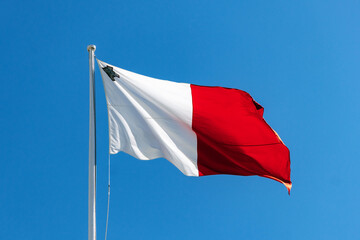 Close-up of the Maltese national flag fluttering in the wind on a sunny day, showing the George Cross and vibrant red and white colors