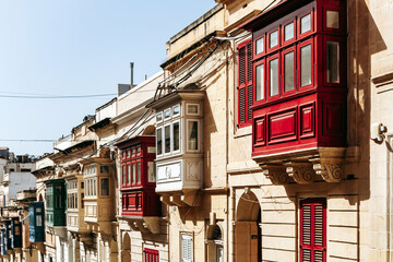 Traditional Maltese wooden balconies painted in vibrant colors on limestone facades, typical...