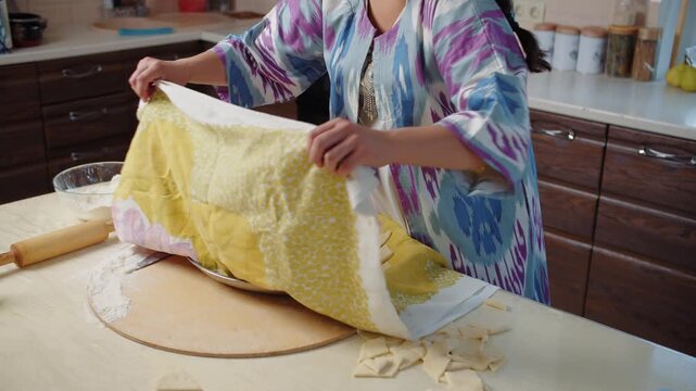 Woman covering baursak dough pieces with kitchen towel