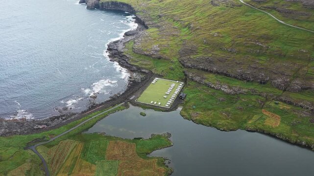 Aerial view of Ei&eth;i Camping nestled between the rugged coastline and a tranquil lake, displaying a dramatic contrast of textures and tones, Ei&eth;i, Eysturoy, Faroe Islands.