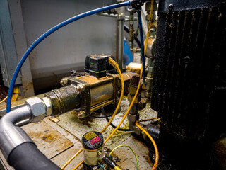 Detailed view of industrial machinery components in a manufacturing setup with visible oil residue and connected hoses