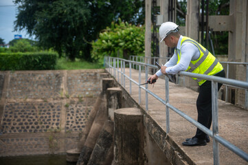 A male dam engineer is checking the water volume in the reservoir and recording it in a document