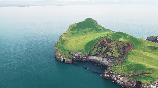 Aerial view of the verdant green Elli&eth;aey island contrasting with the deep blue sea, showcasing the rugged coastline and lone structure, Elli&eth;aey, Vestmannaeyjab&aelig;r, Iceland.