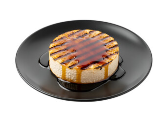 A grilled cheese wheel, drizzled with a rich caramel sauce, sits on a dark plate against a black background.