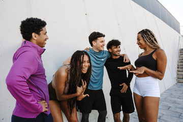 A group of five athletes laughing and talking while standing near a wall