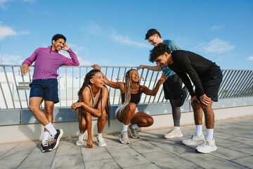 A group of three male athletes stand next to two female athletes who are sitting while they laugh