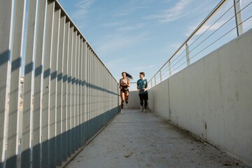 A male athlete looks at a smiling female athlete as they run across a bridge