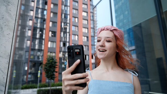A teenage girl poses and smiles for a selfie on a smartphone.