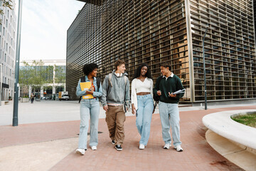 Obraz premium A group of four students are walking and laughing while talking and holding notebooks