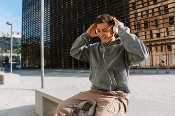 A male student is sitting and smiling while holding his hands on headphones