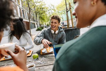 A male student laughs while sitting at a table with a group of three students during lunch