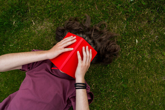 Student relaxing outdoors on grass with book covering face during study break