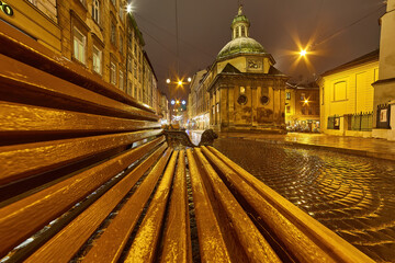 Historic European city square with a wet cobblestone street at night.
