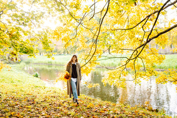 A young woman in a raincoat stands with a bouquet of fallen leaves in an autumn park. A beautiful...
